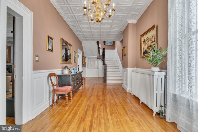 hallway featuring an ornate ceiling, light wood-style floors, radiator heating unit, and stairs