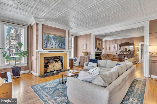 living room featuring radiator, an ornate ceiling, light wood-style flooring, ornamental molding, and a fireplace with flush hearth