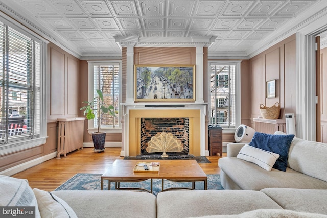 living area featuring an ornate ceiling, a fireplace with flush hearth, light wood-style flooring, and radiator heating unit