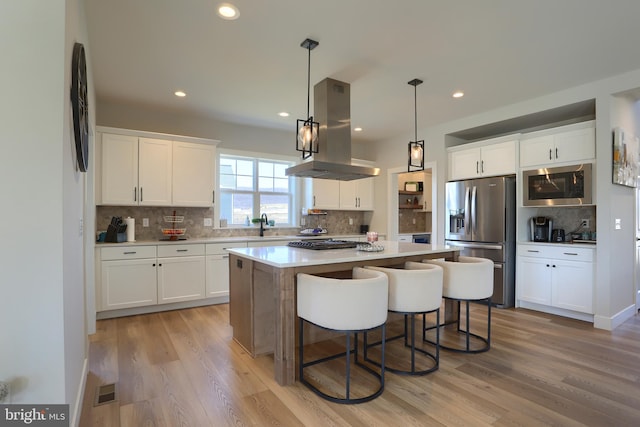 kitchen with stainless steel fridge with ice dispenser, white cabinets, built in microwave, and island range hood