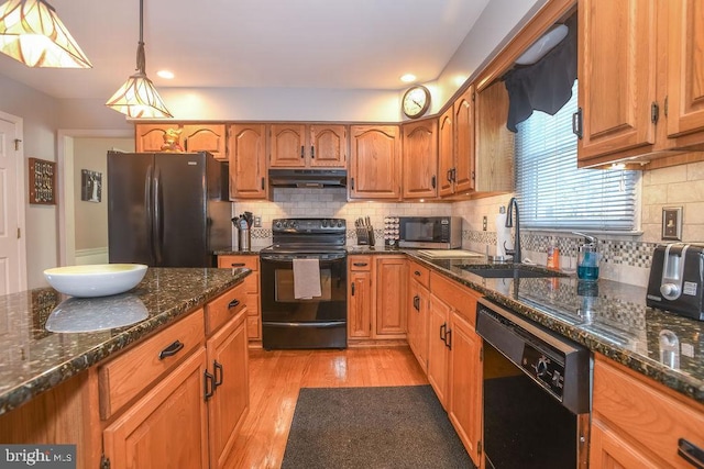 kitchen featuring light wood finished floors, under cabinet range hood, brown cabinets, black appliances, and a sink