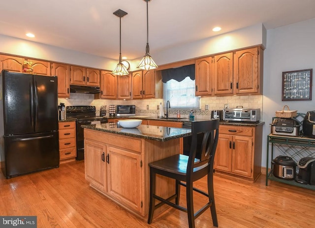 kitchen featuring light wood finished floors, under cabinet range hood, decorative backsplash, black appliances, and a sink