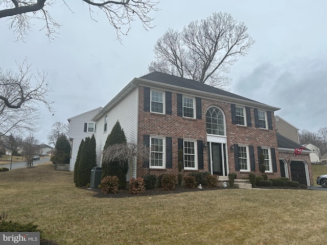 colonial home featuring a front lawn, an attached garage, central AC unit, and brick siding