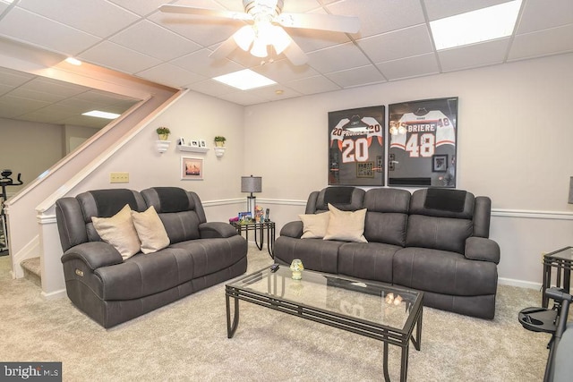 carpeted living area featuring a drop ceiling, baseboards, a ceiling fan, and stairs