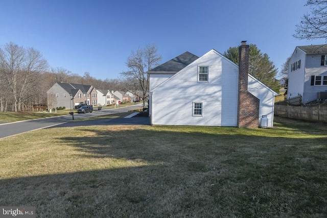 view of side of property featuring a residential view, a chimney, a yard, and fence