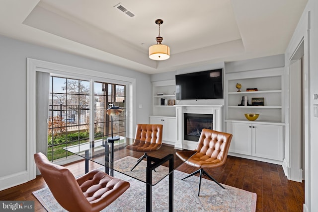 living area featuring a glass covered fireplace, a raised ceiling, and dark wood finished floors