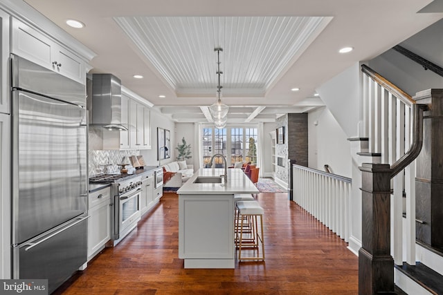 kitchen featuring dark wood finished floors, high end appliances, open floor plan, a sink, and wall chimney exhaust hood