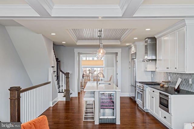 kitchen with high end appliances, wine cooler, a tray ceiling, wall chimney range hood, and a sink