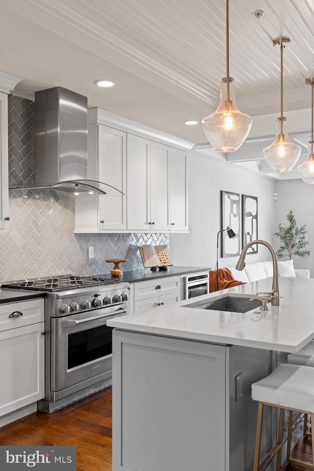 kitchen featuring tasteful backsplash, white cabinets, wall chimney exhaust hood, high end stainless steel range oven, and a sink