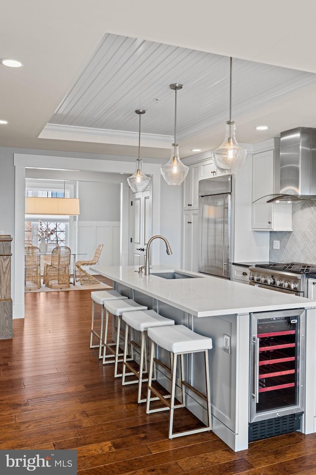 kitchen featuring beverage cooler, dark wood-type flooring, stainless steel built in fridge, wall chimney range hood, and a sink