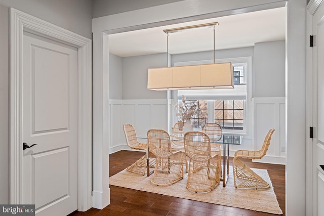 dining area featuring a wainscoted wall, dark wood-type flooring, and a decorative wall