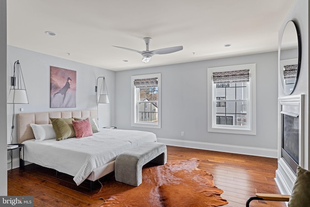 bedroom featuring ceiling fan, recessed lighting, a fireplace, baseboards, and wood-type flooring