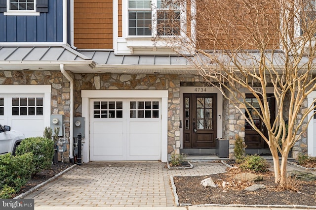 doorway to property with a garage, stone siding, decorative driveway, and board and batten siding