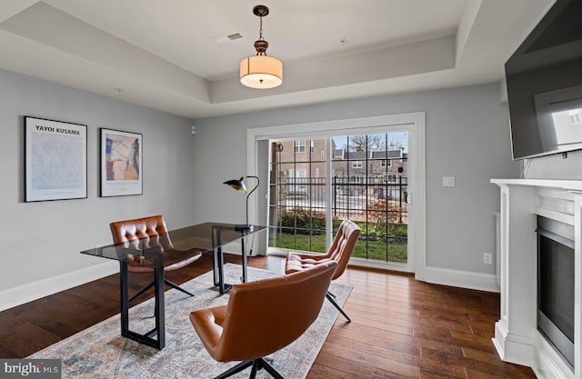 home office featuring a raised ceiling, visible vents, baseboards, and wood finished floors