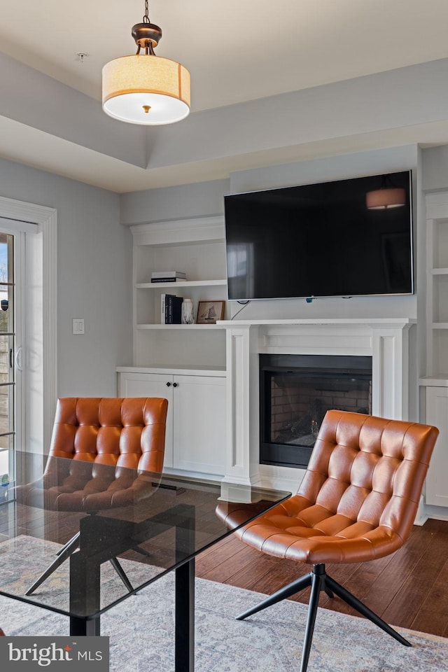 living area with built in shelves, a glass covered fireplace, a tray ceiling, and hardwood / wood-style floors