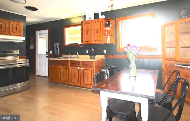 kitchen featuring under cabinet range hood, a sink, brown cabinets, light wood finished floors, and stainless steel range with electric stovetop