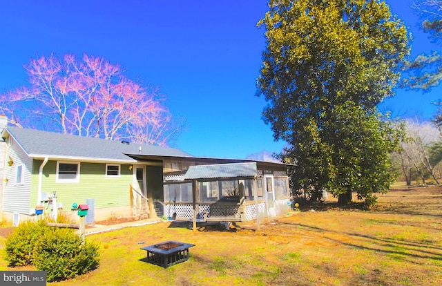 rear view of house featuring a sunroom, a fire pit, and a yard