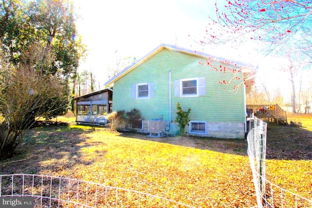 view of property exterior featuring a sunroom, a lawn, and central air condition unit