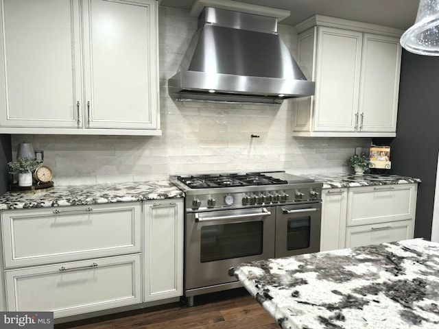 kitchen with wall chimney range hood, range with two ovens, light stone countertops, and tasteful backsplash