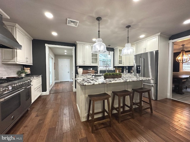 kitchen with wall chimney exhaust hood, high end appliances, glass insert cabinets, and dark wood-style flooring