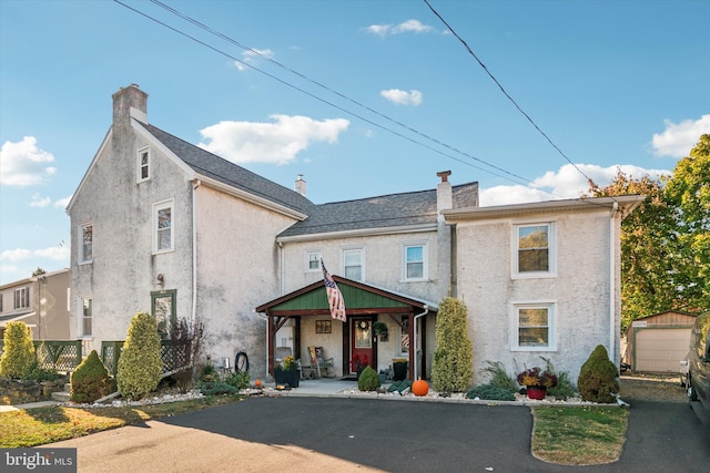 view of front facade featuring driveway, a garage, an outbuilding, covered porch, and stucco siding