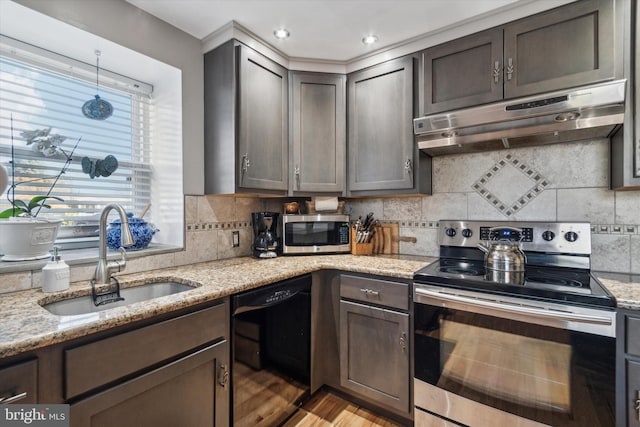 kitchen featuring decorative backsplash, light stone counters, stainless steel appliances, under cabinet range hood, and a sink