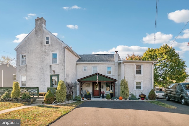 view of front facade with covered porch, a chimney, and stucco siding