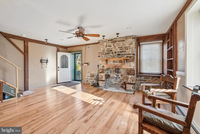 living area featuring ceiling fan, wood finished floors, and a stone fireplace