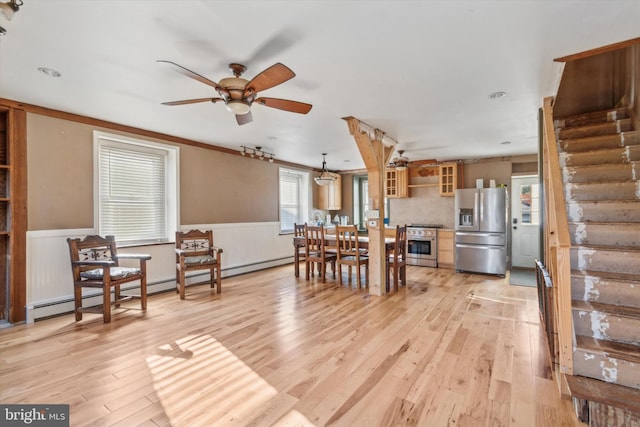 dining space featuring a wainscoted wall, ceiling fan, light wood-type flooring, and stairs