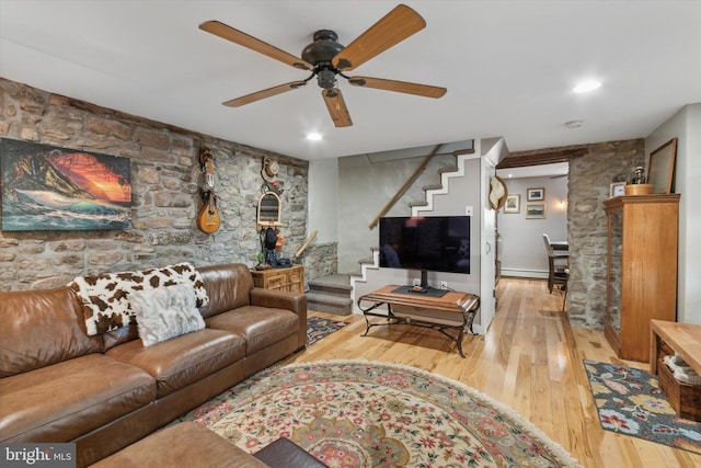 living room featuring a baseboard heating unit, a ceiling fan, stairway, and wood finished floors