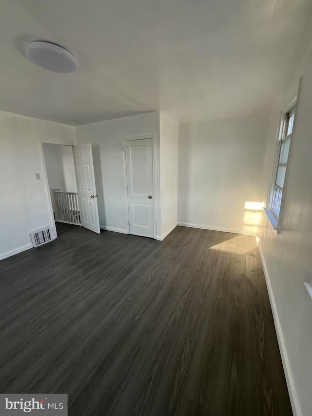 unfurnished room with baseboards, visible vents, and dark wood finished floors