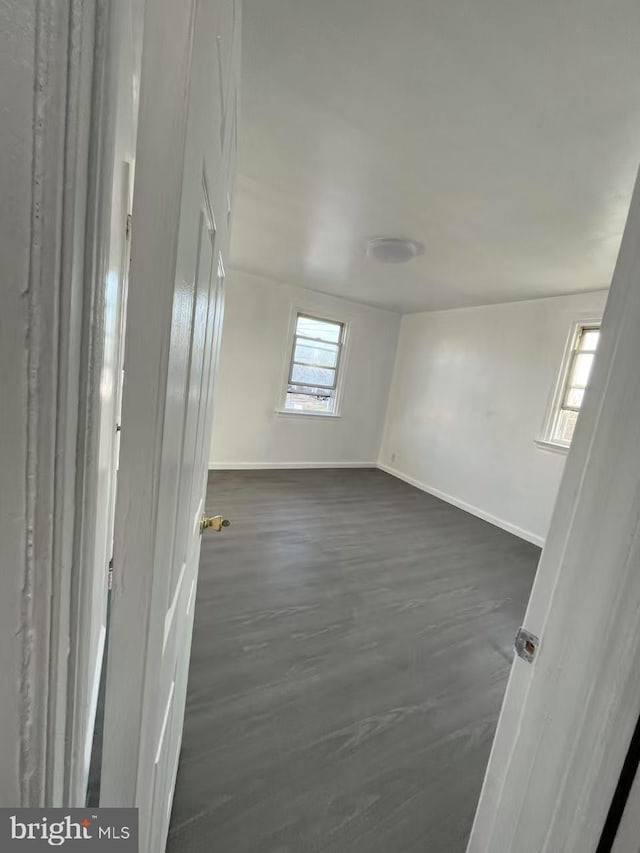 unfurnished room featuring baseboards and dark wood-type flooring