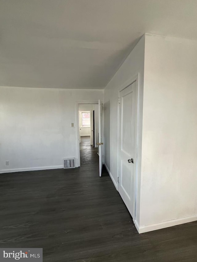 corridor with baseboards, visible vents, and dark wood-style flooring