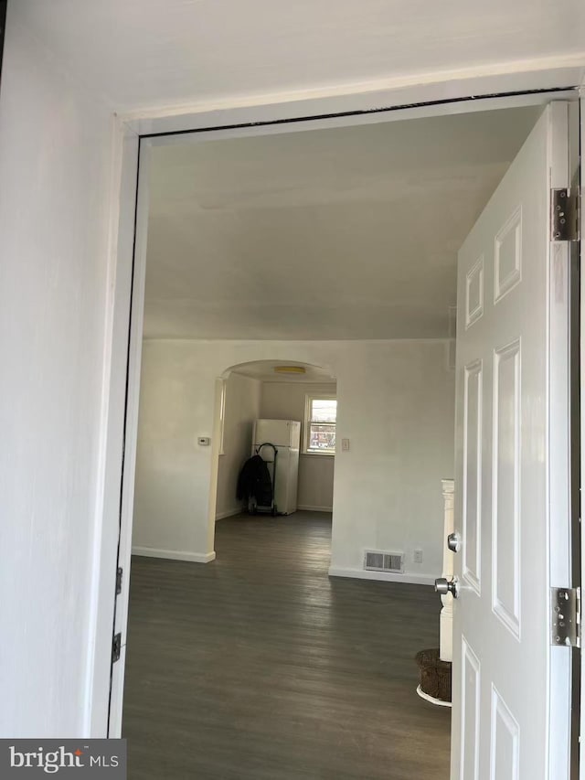 hallway with arched walkways, visible vents, baseboards, and wood finished floors