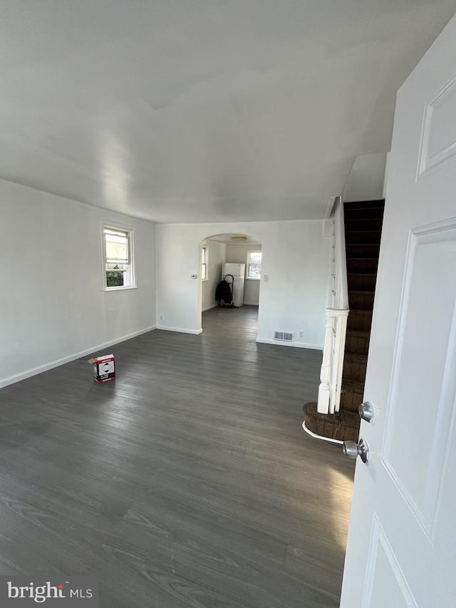 unfurnished living room with baseboards, visible vents, arched walkways, dark wood-type flooring, and stairs