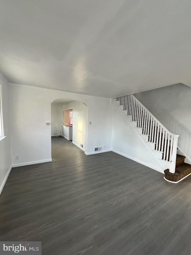 unfurnished living room featuring visible vents, arched walkways, baseboards, dark wood-style floors, and stairway