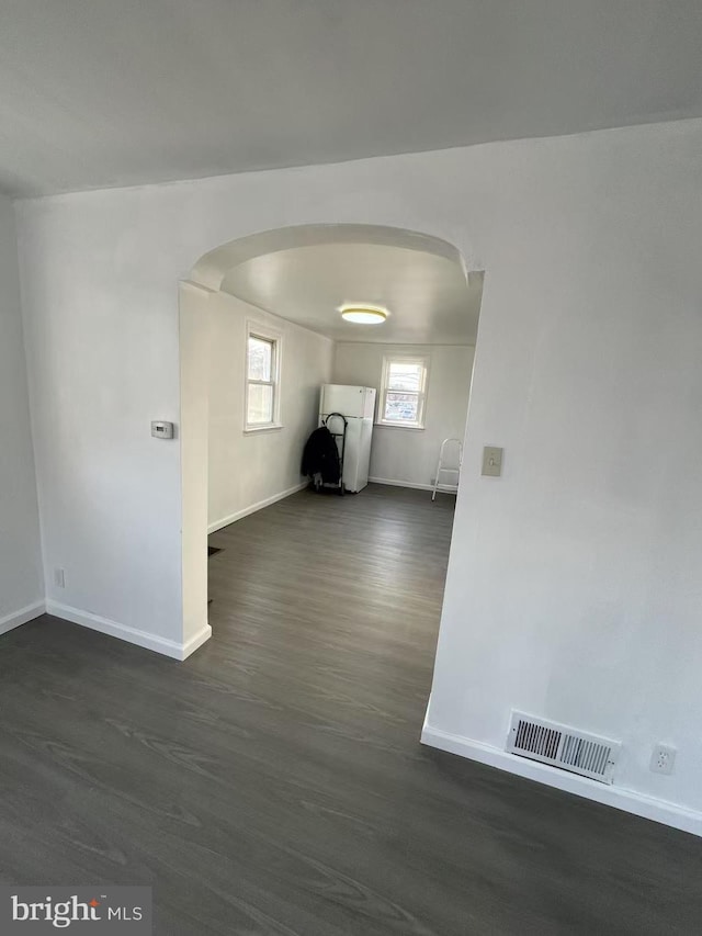 empty room featuring baseboards, visible vents, arched walkways, and dark wood-style flooring