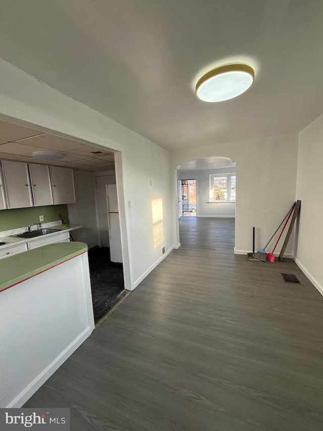 corridor featuring arched walkways, dark wood-style flooring, a sink, visible vents, and baseboards