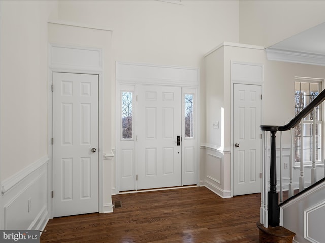 foyer featuring a wainscoted wall, ornamental molding, stairway, and dark wood-style floors