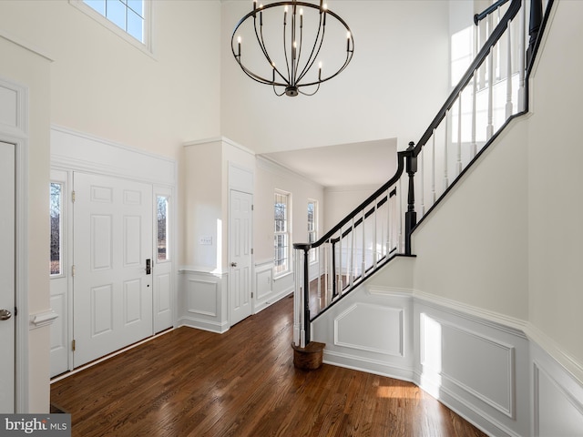 foyer entrance with a decorative wall, dark wood-type flooring, stairway, and a notable chandelier