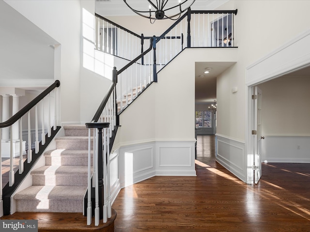 staircase featuring a decorative wall, wood finished floors, a towering ceiling, and a notable chandelier