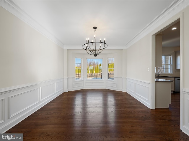 unfurnished dining area featuring a decorative wall, dark wood-type flooring, ornamental molding, a sink, and a chandelier