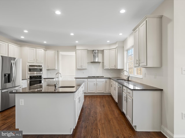 kitchen with an island with sink, wall chimney range hood, stainless steel appliances, and a sink