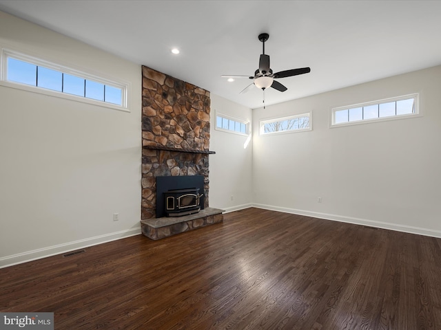 unfurnished living room featuring dark wood-style floors, visible vents, a ceiling fan, a wood stove, and baseboards