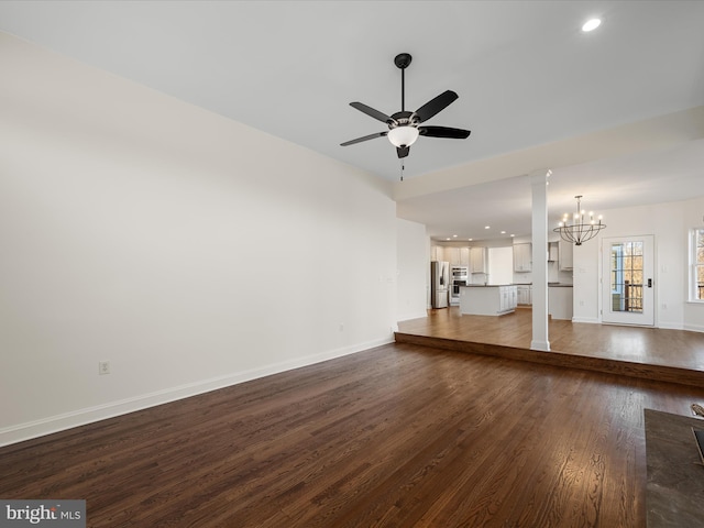 unfurnished living room with ceiling fan with notable chandelier, dark wood-type flooring, recessed lighting, and baseboards