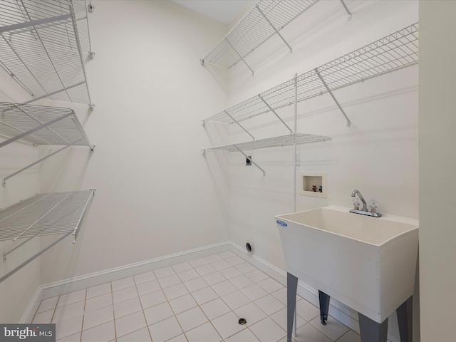 washroom featuring laundry area, baseboards, tile patterned flooring, washer hookup, and a sink