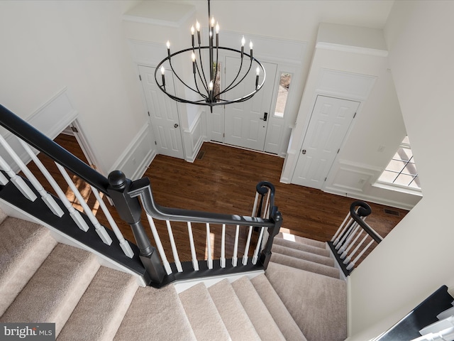 staircase with visible vents, a chandelier, a decorative wall, and wood finished floors