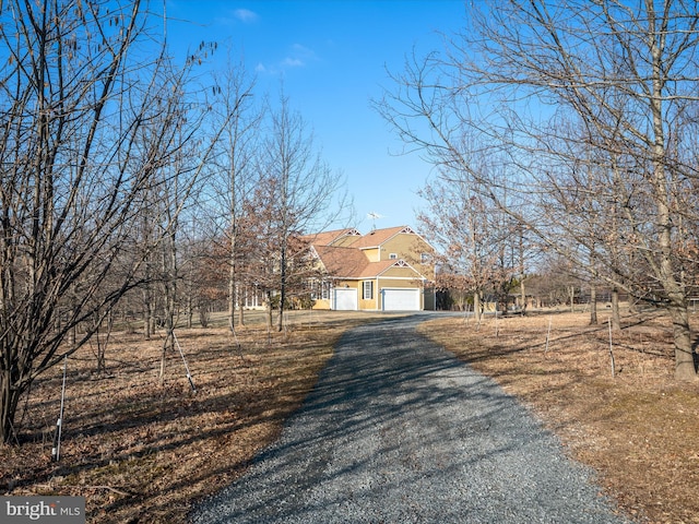 view of front of house with an attached garage, roof with shingles, and gravel driveway