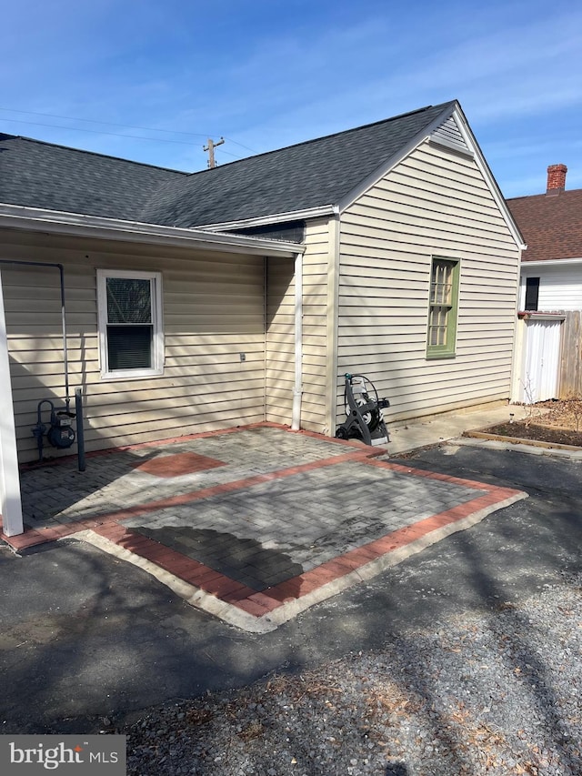 rear view of house featuring roof with shingles and a patio area