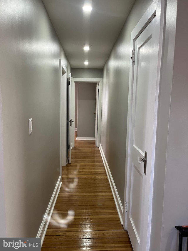 corridor featuring baseboards and dark wood-type flooring